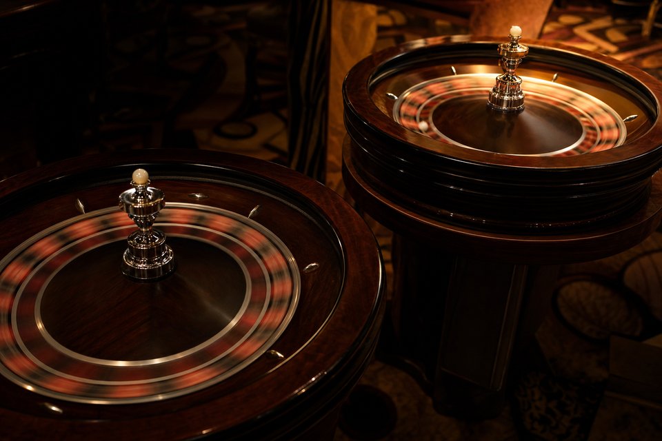 Two roulette wheels side by side on separate tables in a dim casino, both spinning out of focus. (AI-generated image)